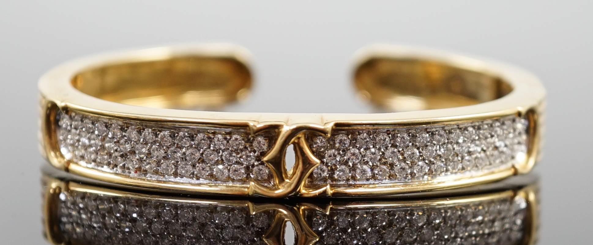 A modern 18k gold and pave set diamond Cartier open work hinged bangle